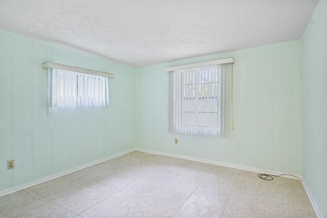 unfurnished room with plenty of natural light, light tile patterned floors, a textured ceiling, and wooden walls