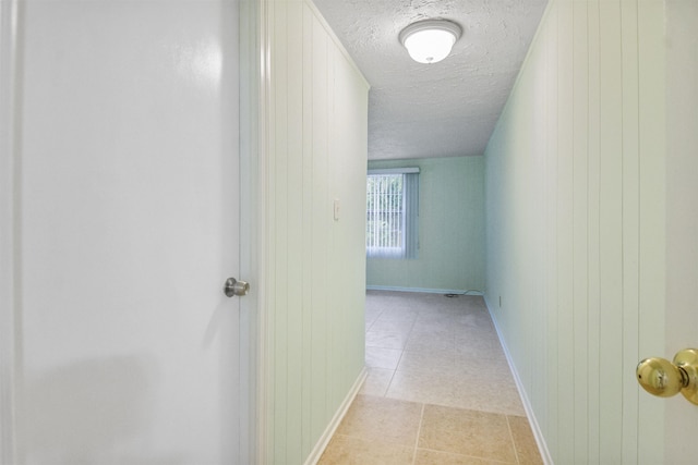 corridor featuring light tile patterned floors, a textured ceiling, and wooden walls