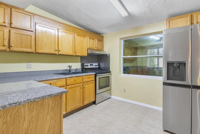 kitchen with a textured ceiling, light stone counters, sink, and appliances with stainless steel finishes