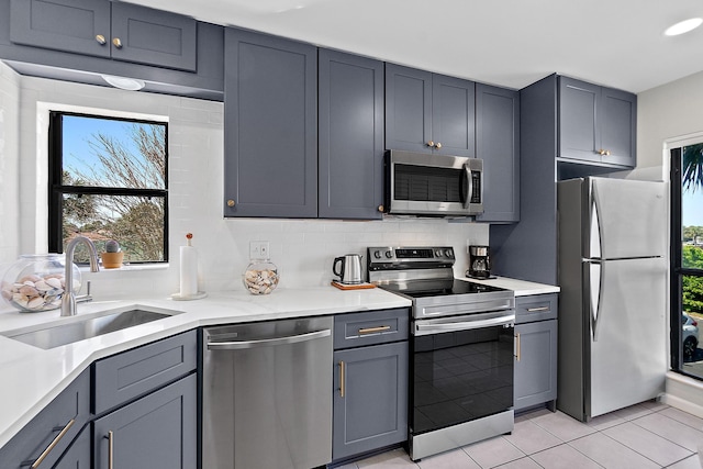 kitchen with light tile patterned floors, a sink, light countertops, appliances with stainless steel finishes, and tasteful backsplash