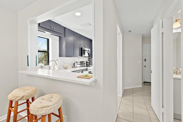 kitchen with light tile patterned floors, light countertops, appliances with stainless steel finishes, a kitchen breakfast bar, and backsplash