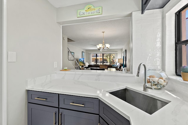 kitchen with light stone countertops, a sink, gray cabinetry, decorative light fixtures, and a notable chandelier