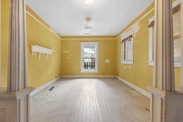 unfurnished room featuring decorative columns and light hardwood / wood-style flooring