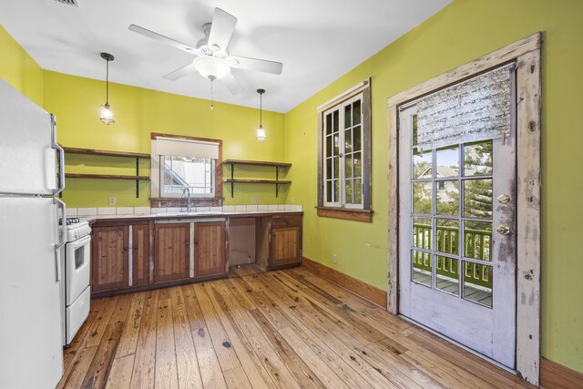 kitchen with light wood-type flooring, white appliances, ceiling fan, sink, and hanging light fixtures