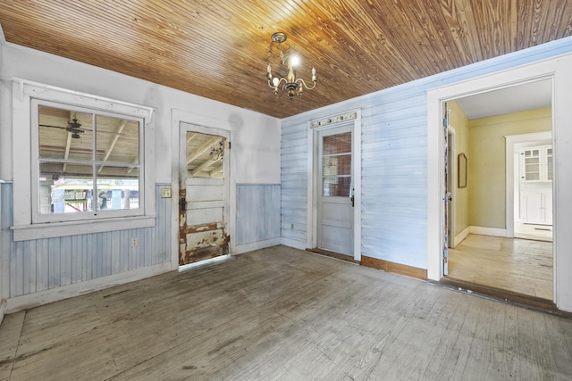 spare room with a chandelier, wood walls, wooden ceiling, and wood-type flooring