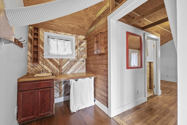 corridor with lofted ceiling, wood-type flooring, sink, and wooden walls