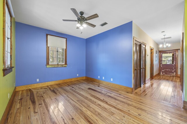 spare room with ceiling fan with notable chandelier and light hardwood / wood-style flooring