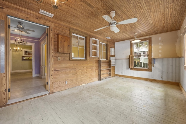 unfurnished living room featuring wood-type flooring, ceiling fan with notable chandelier, wooden ceiling, and wooden walls