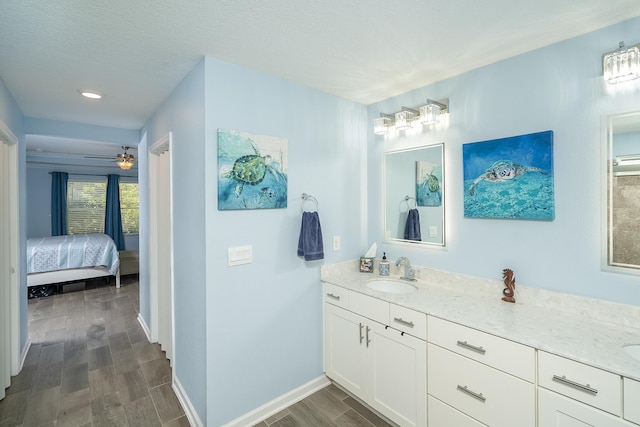 ensuite bathroom featuring a sink, ensuite bath, wood finished floors, double vanity, and baseboards