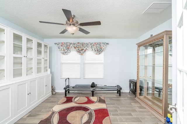 sitting room featuring a textured ceiling, a ceiling fan, visible vents, and wood finish floors