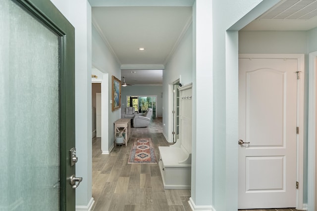 corridor featuring light wood finished floors, visible vents, crown molding, and baseboards