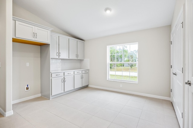 kitchen featuring vaulted ceiling, light tile patterned floors, white cabinets, and backsplash