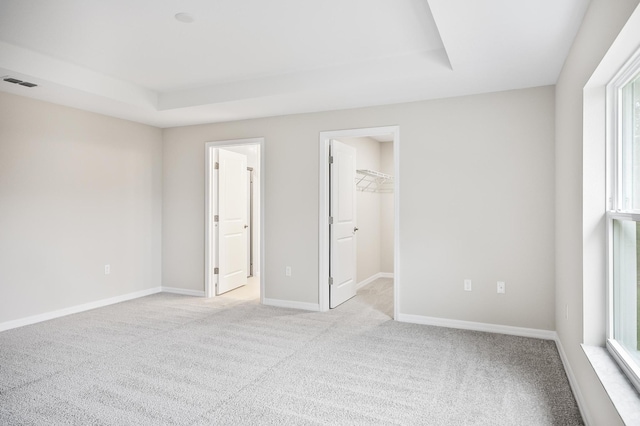 unfurnished bedroom with light carpet, a spacious closet, and a raised ceiling