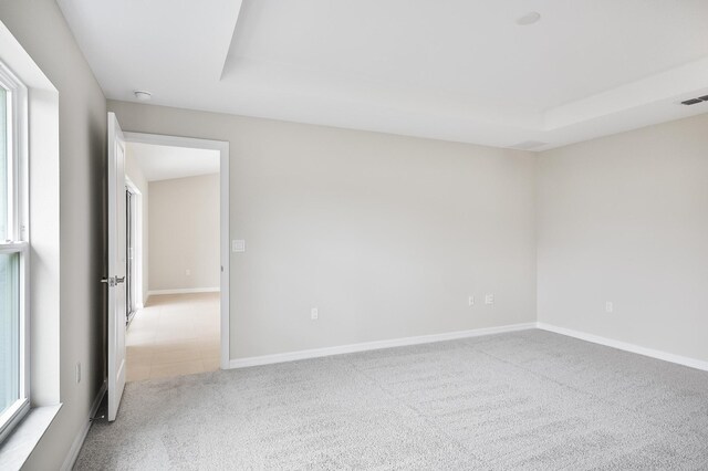 empty room with a raised ceiling and light carpet