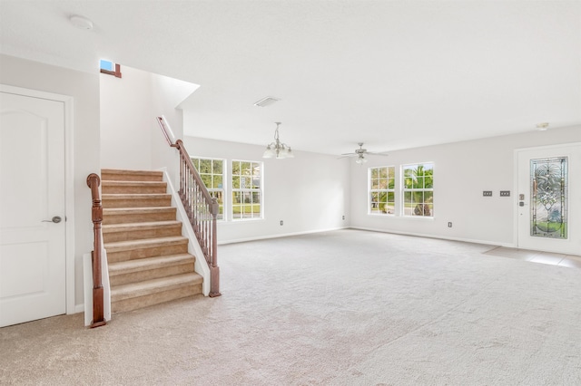 unfurnished living room with ceiling fan with notable chandelier, a healthy amount of sunlight, and light carpet