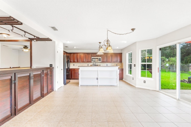 4905 Cypress Links Blvd, Elkton, FL 32033 - kitchen featuring stainless steel microwave, freestanding refrigerator, light countertops, hanging light fixtures, and a center island with sink