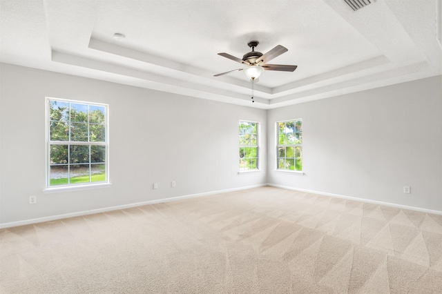 empty room with ceiling fan, light colored carpet, a wealth of natural light, and a tray ceiling