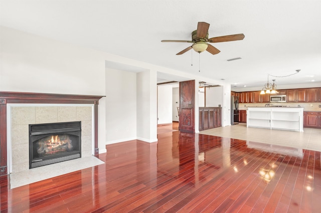 unfurnished living room featuring a tile fireplace, ceiling fan with notable chandelier, and hardwood / wood-style flooring