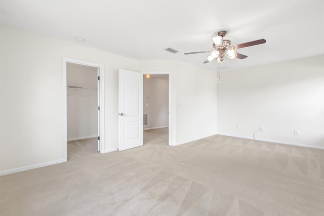 unfurnished bedroom featuring a walk in closet, ceiling fan, a closet, and light colored carpet