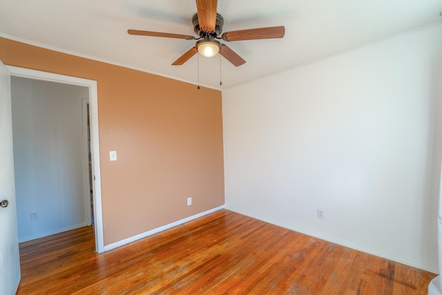 spare room with crown molding, wood finished floors, a ceiling fan, and baseboards