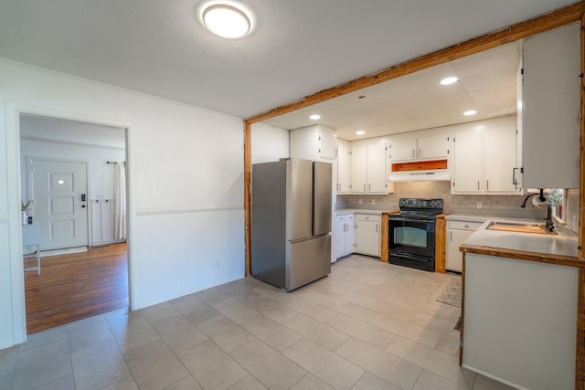 kitchen featuring tasteful backsplash, freestanding refrigerator, a sink, beamed ceiling, and black / electric stove