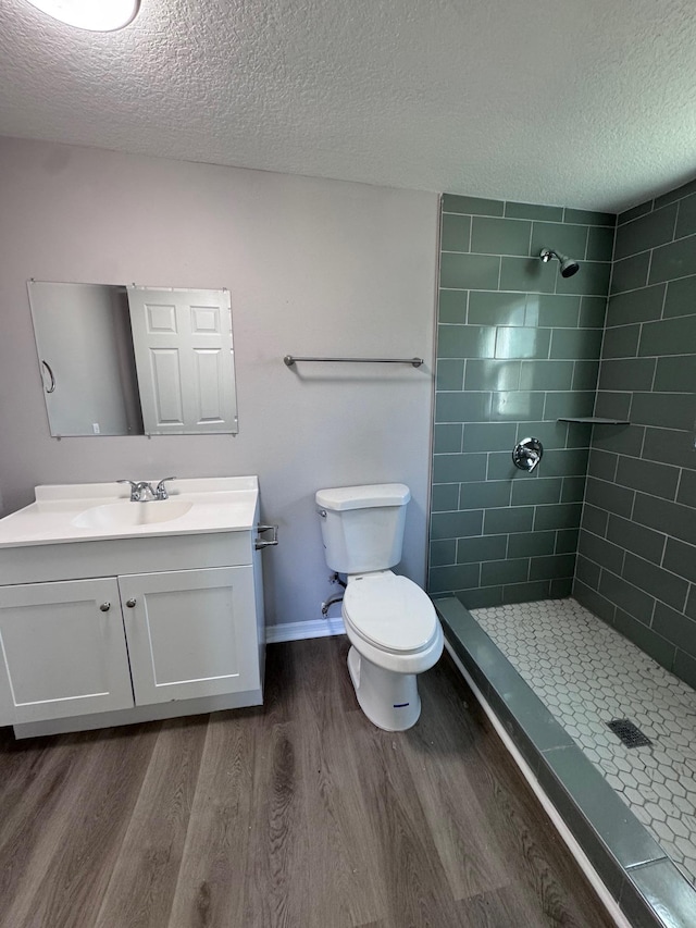 bathroom with hardwood / wood-style flooring, vanity, toilet, and tiled shower