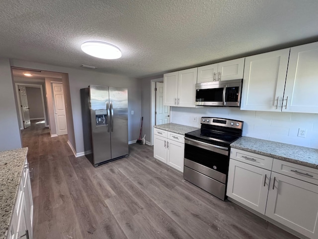 kitchen featuring light stone countertops, a textured ceiling, stainless steel appliances, light hardwood / wood-style flooring, and white cabinets