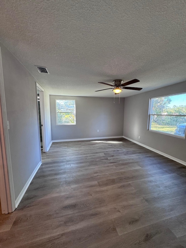 unfurnished room featuring ceiling fan, dark hardwood / wood-style flooring, a textured ceiling, and a wealth of natural light