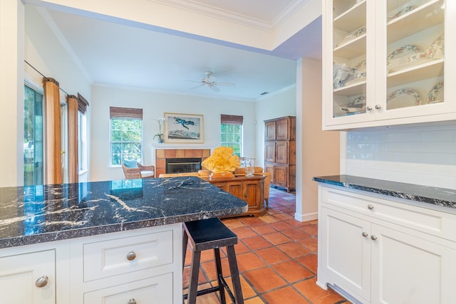 kitchen featuring tasteful backsplash, a fireplace, ornamental molding, ceiling fan, and white cabinets