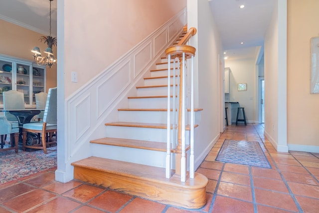 stairs with ornamental molding and a notable chandelier