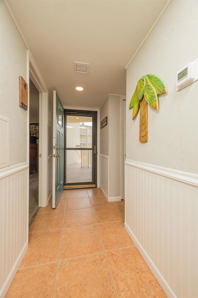 hallway with visible vents, light tile patterned floors, and a wainscoted wall