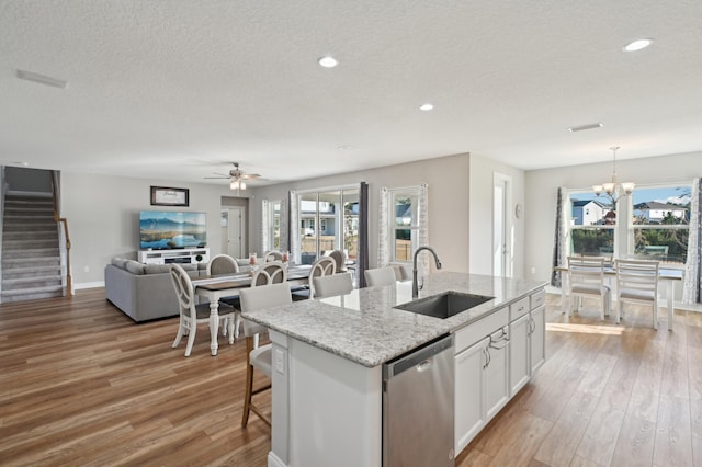 kitchen with pendant lighting, white cabinetry, dishwasher, sink, and a center island with sink