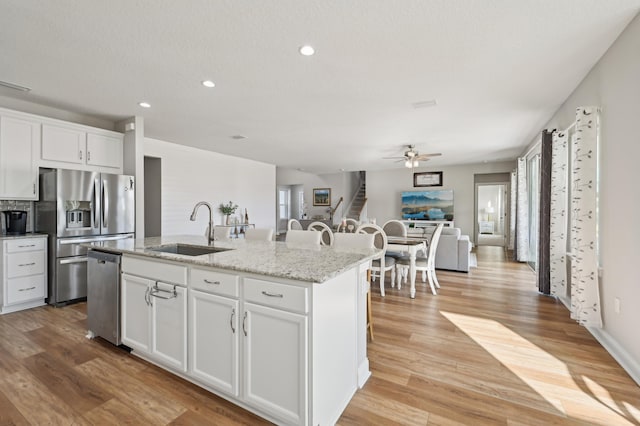 kitchen featuring sink, an island with sink, stainless steel appliances, light stone countertops, and white cabinets