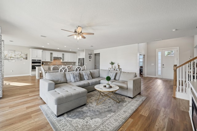 living room featuring ceiling fan, a textured ceiling, and light hardwood / wood-style flooring