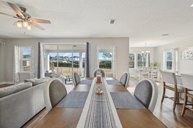 dining room with wood-type flooring, ceiling fan with notable chandelier, and a textured ceiling