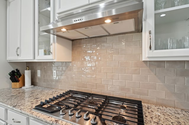 kitchen with stainless steel gas cooktop, extractor fan, white cabinetry, light stone countertops, and backsplash