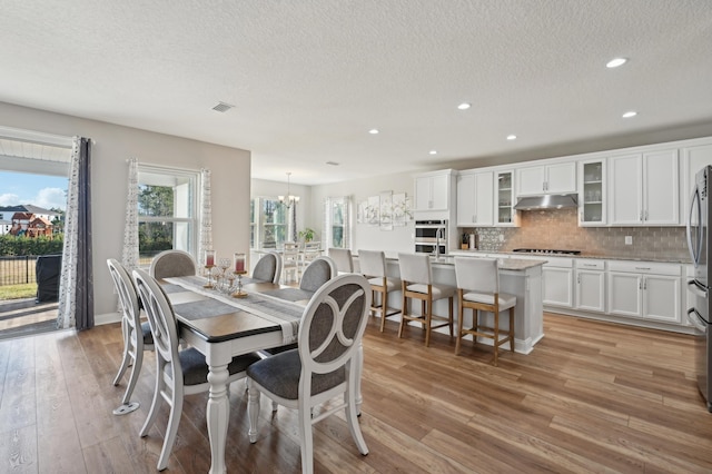 dining room featuring light hardwood / wood-style floors, a textured ceiling, and a notable chandelier