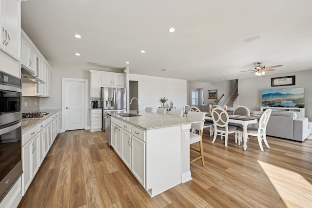 kitchen with an island with sink, sink, white cabinets, backsplash, and light stone countertops