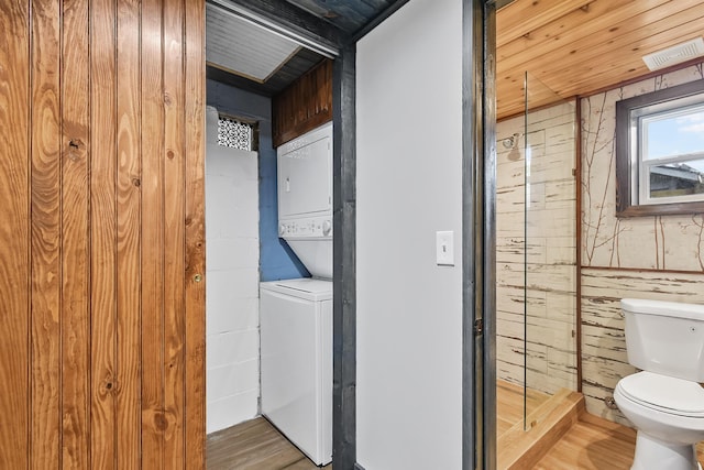 laundry area featuring estacked washer and dryer, wood walls, and wood finished floors