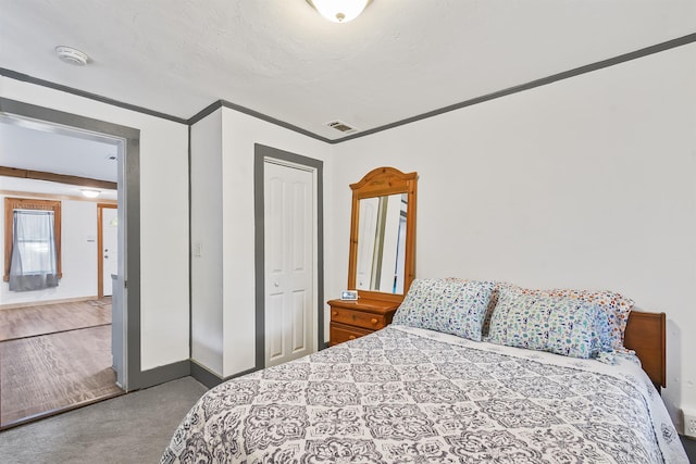 carpeted bedroom with a closet, baseboards, and crown molding