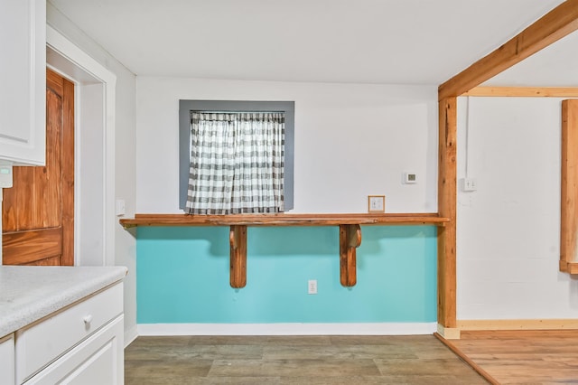 kitchen featuring wood finished floors, white cabinets, baseboards, a breakfast bar, and light countertops
