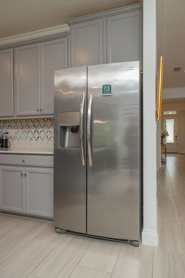 kitchen with tasteful backsplash, ornamental molding, stainless steel fridge, and gray cabinets