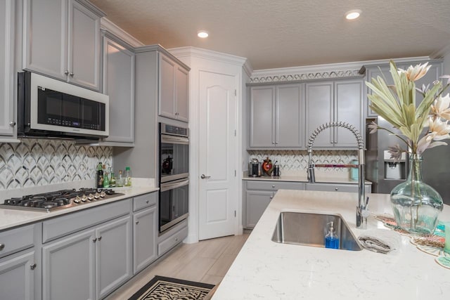 kitchen with sink, tasteful backsplash, a textured ceiling, appliances with stainless steel finishes, and gray cabinets