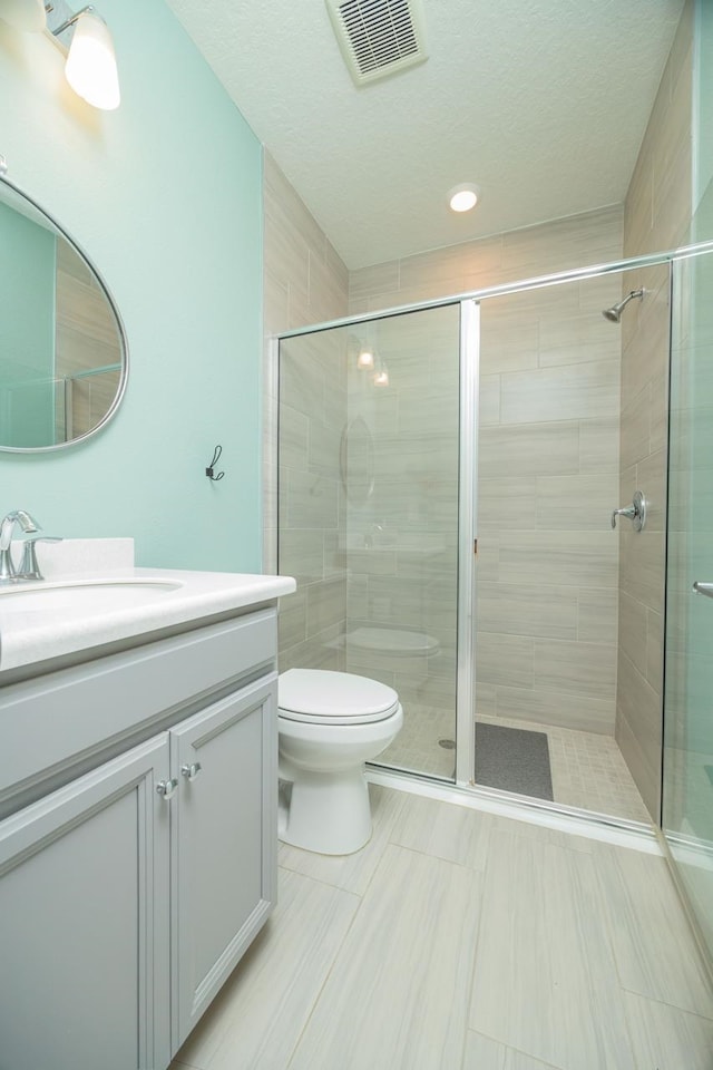 bathroom with vanity, toilet, a shower with door, and a textured ceiling