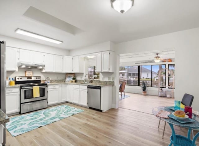 kitchen featuring stainless steel appliances, white cabinets, a sink, light wood-type flooring, and under cabinet range hood