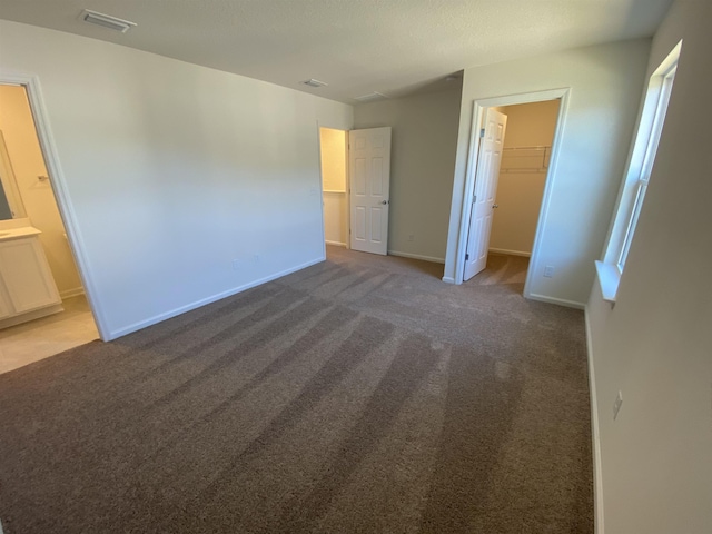 unfurnished bedroom with ensuite bath, a spacious closet, dark carpet, and a closet