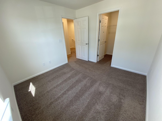 unfurnished bedroom with dark carpet, a spacious closet, and a closet