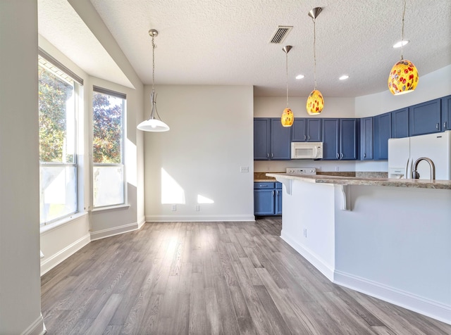 kitchen featuring white appliances, a kitchen breakfast bar, blue cabinets, and visible vents