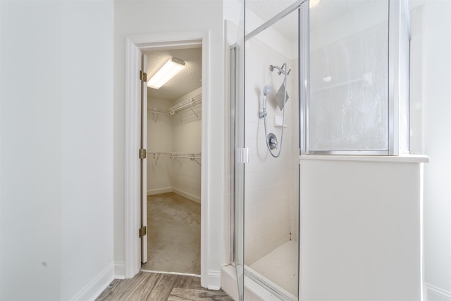 bathroom featuring a walk in closet, a textured ceiling, wood finished floors, a shower stall, and baseboards