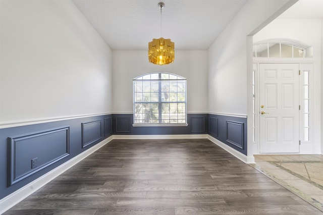 entryway with a textured ceiling, wood finished floors, a wainscoted wall, and a chandelier